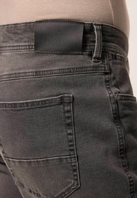 Szare dżinsy z denimu z skórzaną metką wytłoczoną napisem "BOSTON PARK", z widocznym przeszyciem i detalem tylnej kieszeni.