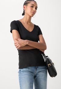Black short-sleeve V-neck t-shirt paired with light blue jeans and a black handbag. The t-shirt has a smooth texture and fitted design.