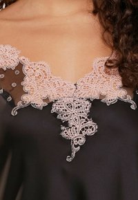 Tessuto nero con scollatura a V profonda, caratterizzato da intricati ricami in pizzo rosa. I motivi del pizzo includono swirl e accenti floreali lungo il collo.