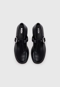 Black leather T-bar shoes with rounded toes, a buckle strap, and a flat sole. Inside features a branded insole in white.