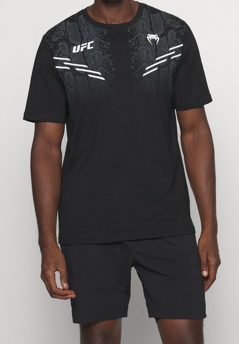 T-shirt de sport noire avec un design texturé dans un motif dégradé, présentant des accents blancs et le logo de l'UFC sur le devant. Associé à un short noir.