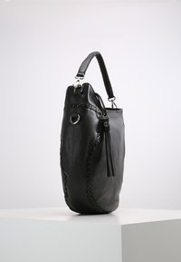 Czarna skórzana torebka z plecionym detalem po boku, z uchwytem na górze i frędzlami jako akcentem. Gładka tekstura z minimalną ilością okucia.