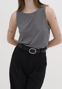 Top de tirantes gris con canalé y escote redondo, combinado con pantalones negros de cintura alta y un cinturón negro con una hebilla plateada.