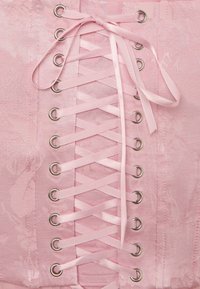 Gros plan d’un corset rose en satin avec des œillets argentés et un laçage en ruban de satin croisé à l’avant.