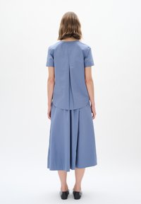 Maglietta in cotone blu con maniche corte e piega sulla schiena, abbinata a una gonna fluida. Design minimalista, tessuto leggero e lunghezza al ginocchio.