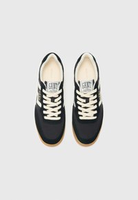Black sneakers with a suede and textile upper, cream laces, and a gum rubber outsole. "GANT" logo displayed on the tongue and side.