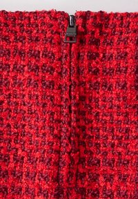 Röd vävd tyg med en texturerad mönstring. Inkluderar en svart dragkedja bak, sömlöst integrerad i designen.