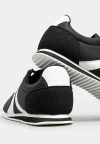 Black and white athletic shoes with a textured black suede heel, smooth black upper, and white accents in a classic running design.