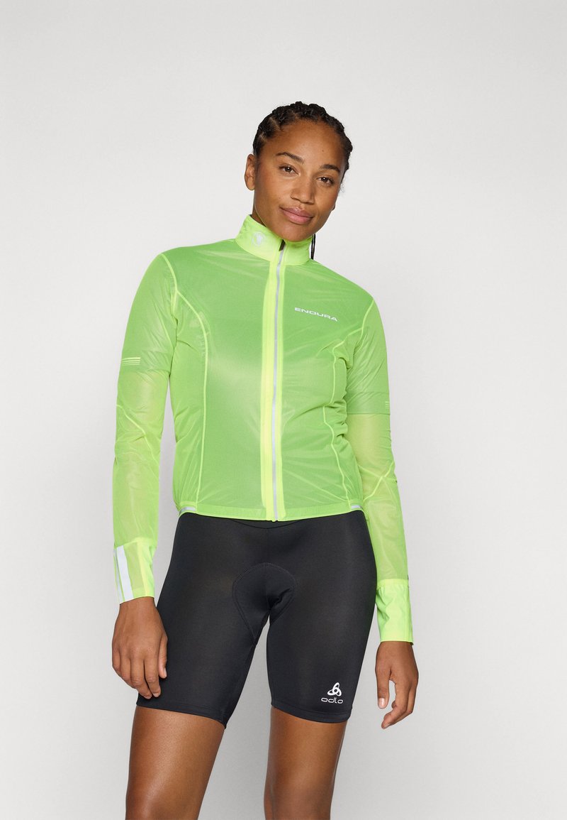 Giacca da ciclismo leggera a maniche lunghe di colore verde fluorescente, con colletto alto, zip frontale e riflessi; abbinata a pantaloni ciclismo neri.