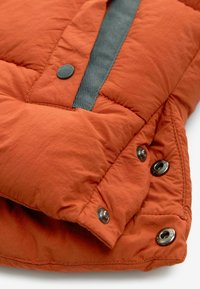 Matière de doudoune orange avec une texture froissée. Présente un accent en tissu gris et des boutons-pression métalliques le long du bord pour la fermeture.