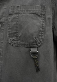 Γκρι υφασμάτινο σακάκι με τσέπη στο στήθος, ενισχυμένες ραφές και μαύρο κλιπ με κίτρινες λεπτομέρειες. Υφή με ανθεκτικό υλικό.