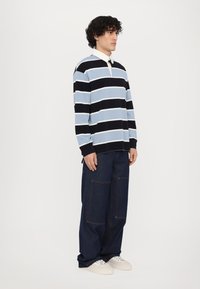 Stripet polo skjorte i lyseblå, marineblå og hvit, med lange ermer og krage. Kombinert med mørkeblå, løstsittende jeans og hvite joggesko.