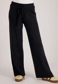 Zwarte, wijd uitlopende broek met een trekkoord in de taille. Gemaakt van zacht materiaal, met een gladde textuur en een casual ontwerp.