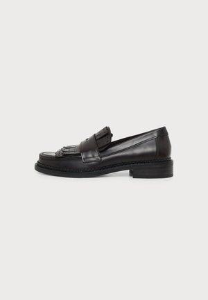 Mocassin en cuir noir avec des détails à franges sur le dessus, talon bas et semelle cousue, montré de côté sur un fond uni.