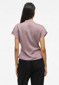 Blusa a maniche corte di un leggero rosa, realizzata in un tessuto liscio simile alla seta con un delicato lucido; presenta un colletto classico e una vestibilità rilassata.