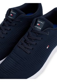 Baskets en textile bleu marine avec une surface texturée, dotées de lacets noirs et d'une semelle blanche. Patte logo sur la languette avec des accents rouges et blancs.