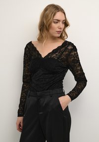 Top in pizzo nero con maniche lunghe, caratterizzato da motivi floreali, una scollatura a V e una silhouette aderente, abbinato a pantaloni neri in satin.