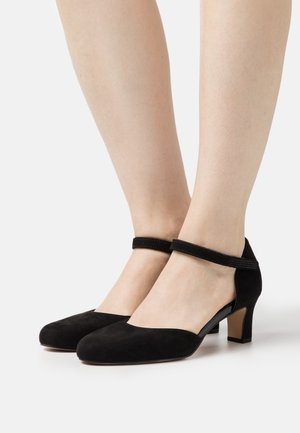 Escarpins en suede noir à talon bas. Dotés d'une bride de cheville avec un accent texturé et d'un léger design découpé sur les côtés.