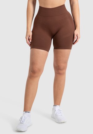Bruine high-waisted performance shorts met een gladde textuur en versterkte naden, gecombineerd met witte sportschoenen.