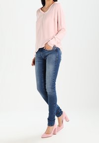 Ljusrosa långärmad topp med v-ringning och rynkade axeldetaljer, stylar med mörkblå skinny jeans och rosa högklackade skor.