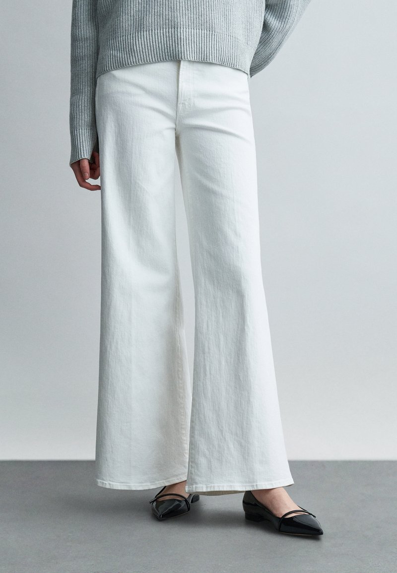 Λευκό παντελόνι από βαμβάκι με φαρ διά παντελόνια και καθαρή υφή. Συνδυασμένο με μαύρα φλατ παπούτσια με μυτερή μύτη και ελάχιστες λεπτομέρειες.