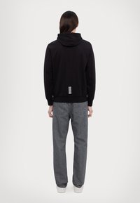 Svart huvtröja med dragsko, ribbade ärmmuddar och en vitrandig detalj på baksidan. Kombinerad med grå, löst sittande jeans och vita sneakers.