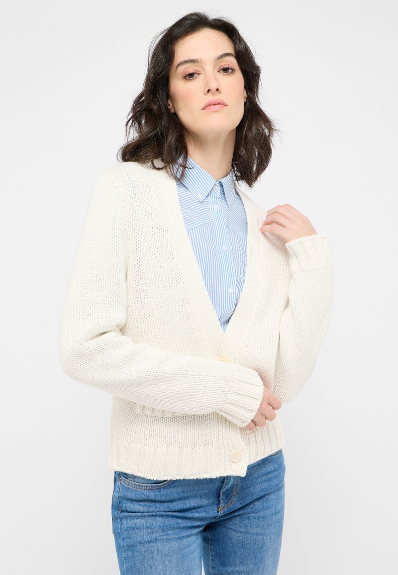 Krämfärgad stickad cardigan med V-ringning, ribbade muddarna och kanten, med två framknappar. Bärs över en blårandig skjorta.