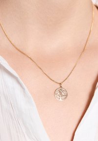 Złoty naszyjnik z łańcuszka z okrągłym wisiorkiem z motywem drzewa, gładką teksturą i misternymi szczegółami wycięcia.