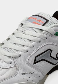 Λευκό αθλητικό παπούτσι με υφή δερμάτινου επάνω μέρους, με αντιθετικές μαύρες και γκρι λεπτομέρειες, επίπεδα κορδόνια και λογότυπο στο πλάι.