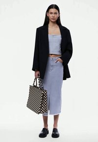 Blazer negro sobre un top corto a rayas azul claro y una falda a juego. Bolsa de mano a cuadros negra y beige, combinada con zapatos negros sin hebilla.