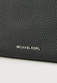 Borsa in pelle nera testurizzata con logo "Michael Kors" in argento. Vista ravvicinata che mette in evidenza il materiale e i dettagli.