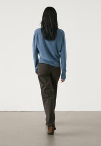 Pull bleu tricoté avec col rond, manches longues et coupe légèrement ample, associé à un pantalon large marron foncé et des chaussures marron.