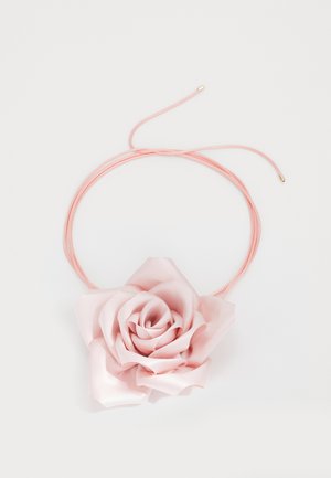 Lyserød satin rose vedhæng på en tynd, lyserød snor med gyldne ender. Blomsten har lagdelte kronblade med en glat overflade og subtil glans.