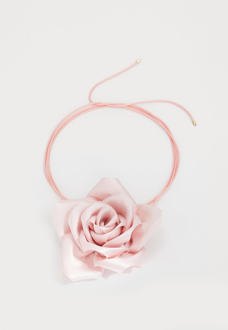 Vaaleanpunaisesta satiinista valmistettu ruusuketju ohuehkolle vaaleanpunaiselle narulle, jonka päässä on kultaiset päät. Kukassa on kerroksellisia terälehtiä, joissa on sileä pinta ja hienovarainen kiilto.