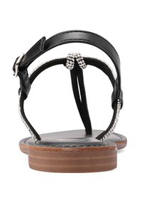 Sandalo in pelle nera con suola piatta, con un design a T-strap decorato con perline e un tacco in legno marrone. Fascetta alla caviglia regolabile per una vestibilità ottimale.