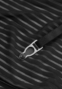 Tissu noir transparent avec des rayures horizontales, comportant un fermoir en métal et une sangle noire lisse. La surface texturée ajoute de la dimension.