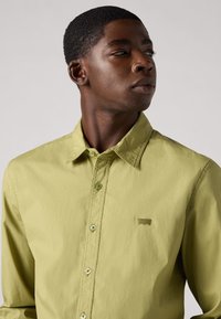 Camicia button-up verde chiaro con colletto, caratterizzata da un sottile logo del marchio sul petto e bottoni abbinati, realizzata in un tessuto morbido.