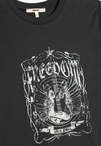 Camiseta negra de algodón con un gráfico blanco desgastado de una guitarra con alas, el texto "LIBERTAD" y "ROCK & ROLL", y bordes intrincados.