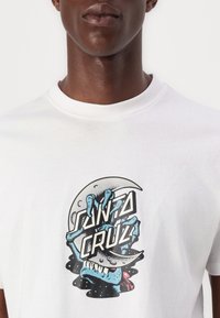 White cotton T-shirt featuring a graphic design of a blue hand clutching a half-moon with "SANTA CRUZ" text in bold black letters.