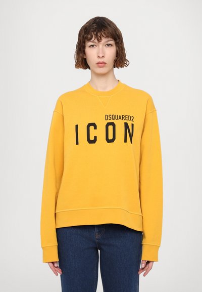 Sweatshirt jaune à col rond et manches longues. Texte noir "ICON" sur le devant. Texture douce, coupe décontractée, ourlet légèrement plus long à l'arrière.