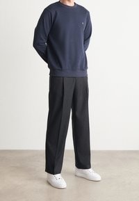 Námořnická mikina s žebrovanými manžetami a výstřihem, spárovaná s černými skládacími kalhotami a bílými teniskami. Hladká textura a minimální značení.