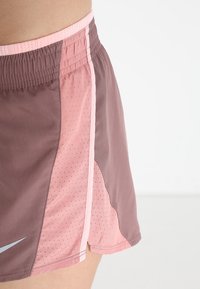 Braune und pinke Sportshorts mit Netzstruktur, seitlichem Schlitz und weißen Akzenten. Elastischer Bund für eine verstellbare Passform.