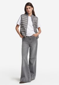 Szary kamizelka puchowa o pikowanej fakturze, noszona na białym T-shircie i dopasowana do szerokich szarych dżinsów. Luźny styl z prostym wzornictwem.