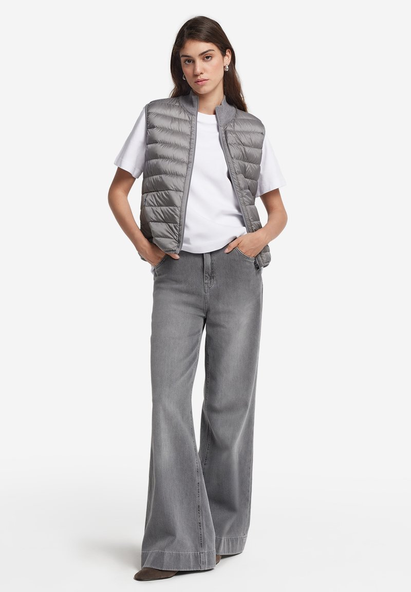 Szary kamizelka puchowa o pikowanej fakturze, noszona na białym T-shircie i dopasowana do szerokich szarych dżinsów. Luźny styl z prostym wzornictwem.