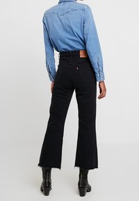 Pantalones vaqueros anchos negros con dobladillo deshilachado, cintura alta y parche de cuero en la parte posterior. Combinados con una camisa de mezclilla azul clara.