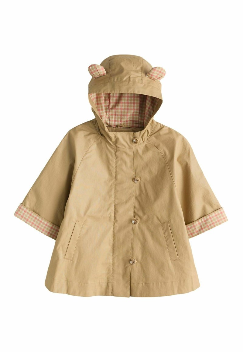 Bezs esőkabát kapucnival, melynek kapucniján macifülek vannak, kockás bélés és kockás mandzsetták. Elöl gombokkal és oldalsó zsebekkel rendelkezik. Vízhatlan anyagból készült.
