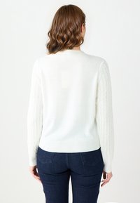 White sweater with textured cable-knit sleeves, ribbed cuffs and hem. Back view shows smooth fabric and classic crew neck design.