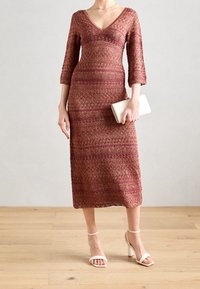 Robe mi-longue en V couleur bordeaux avec tricot texturé et motif. Assortie à des talons ouverts blancs et un petit sac à main.