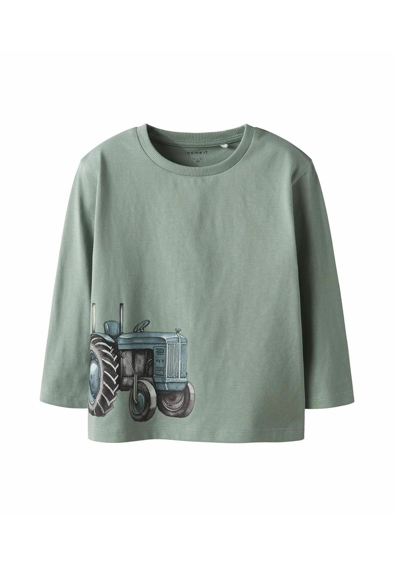 Zaļš garām piedurknēm T-krekls ar apaļu kakla izgriezumu un traktora grafikas printu zilā un pelēkā krāsā apakšpusē. Izgatavots no kokvilnas auduma.