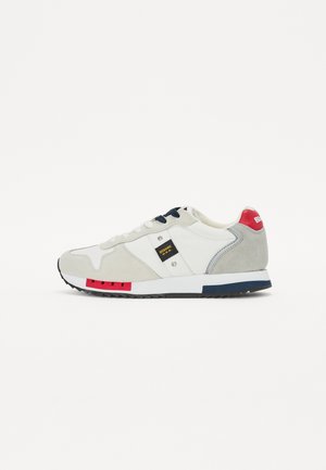Zapatillas con parte superior de nylon blanco, detalles en ante gris, cordones azul marino, suela con detalles en rojo y azul, y un pequeño parche de logo negro.